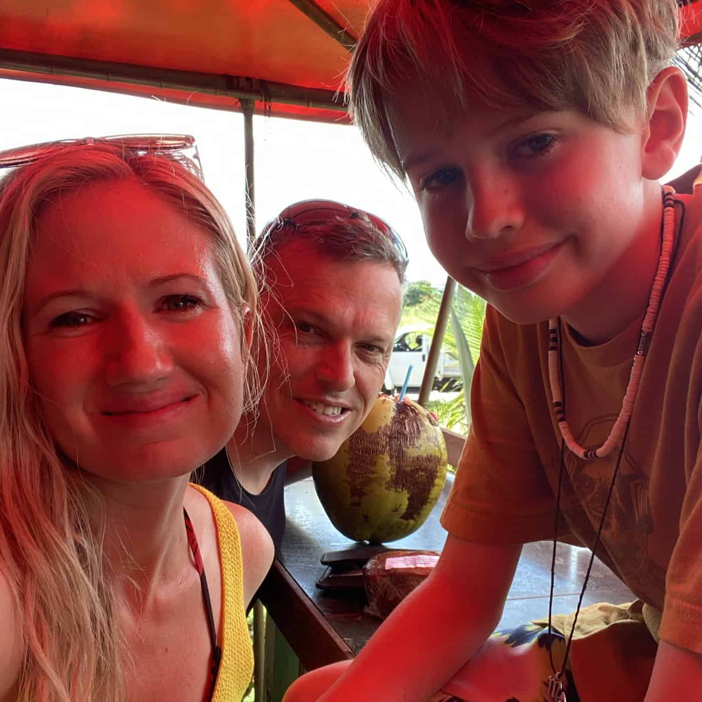 A blonde woman in a yellow shirt, man in a black shirt and boy wearing a shell necklace smiling